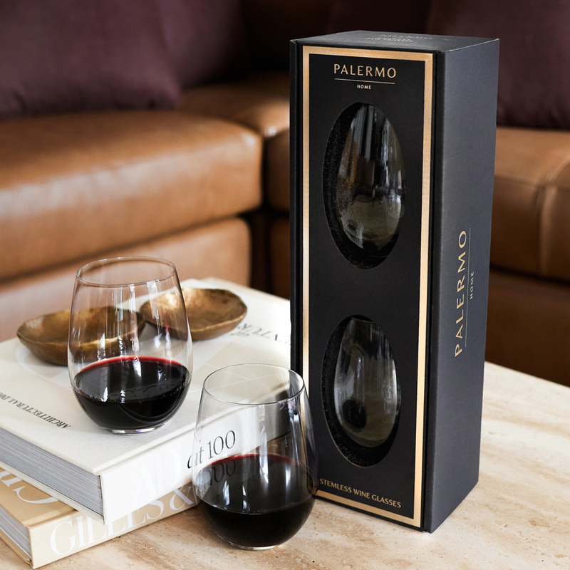 Two wine glasses with red wine next to a black 'Palermo' packaging box on a wooden surface.