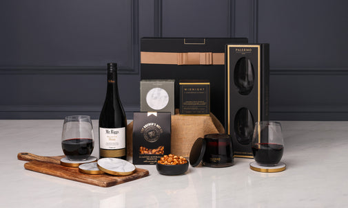 Wine bottle, glasses, and snacks on a table with a dark background