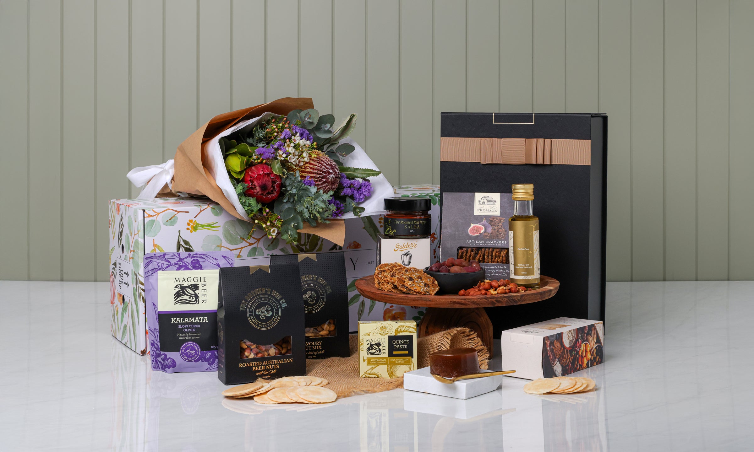 Gourmet gift basket with flowers, snacks, and a bottle on a white surface.