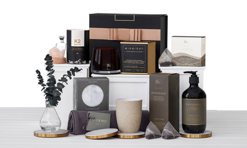 A collection of homeware items including decorative and functional products such as framed art prints, candles, and bath products, displayed in a gift hamper.